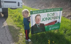 A very young man holds an electric screwgun to put up Bob Jonkman's sign